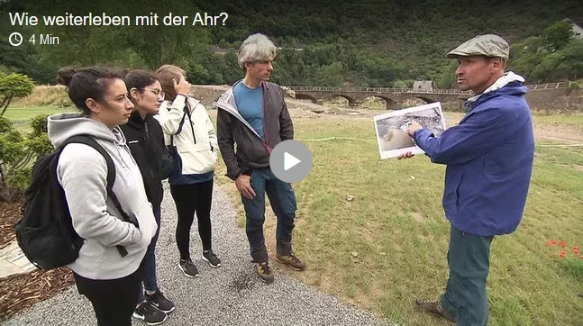 Eine Wissenschaftlerin und ein Wissenschaftler arbeiten hinter einer Glasfassade und mischen Chemikalien mit Großgeräten.