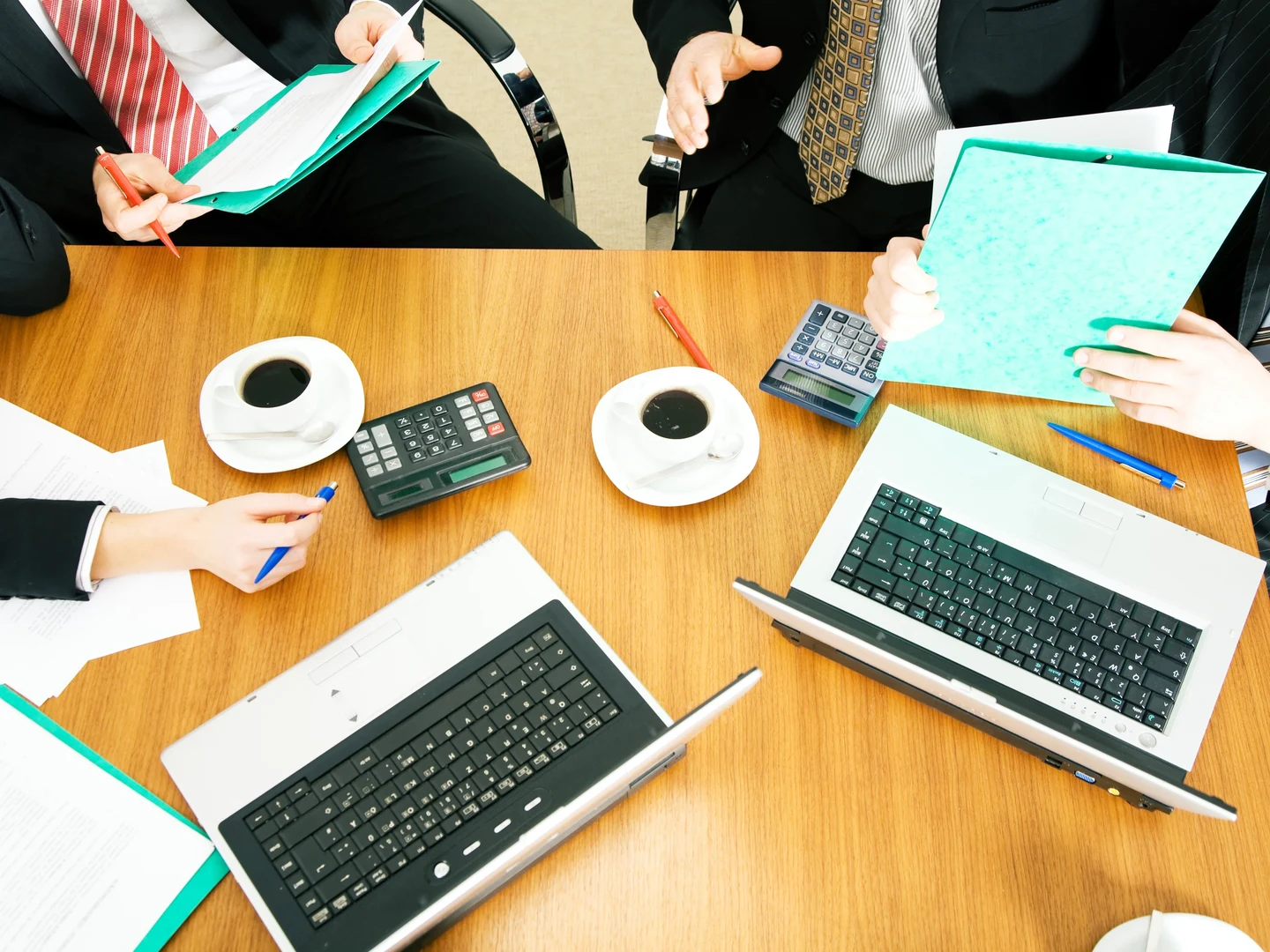 Drei Personen im Gespräch mit Akten in der Hand und Laptops und Kaffeetassen auf dem Tisch vor ihnen