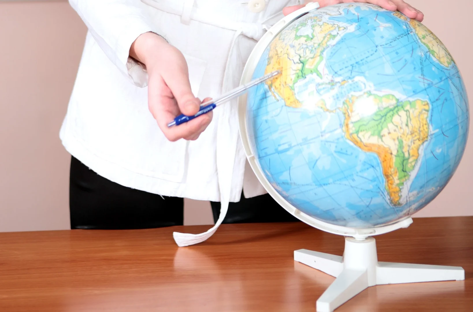 Person die mit einem Stift auf einen Globus zeigt
